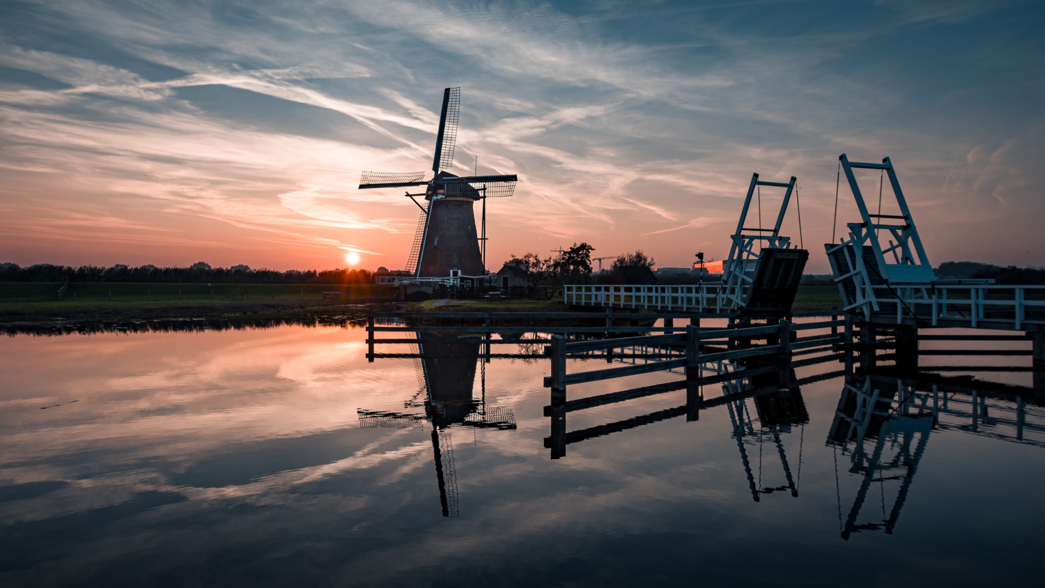 Windmühle und Zugbrücke in Kinderdijk bei Sonnenuntergang mit Spiegelungen auf der Wasseroberfläche
