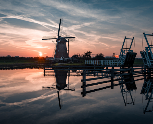 Windmühle und Zugbrücke in Kinderdijk bei Sonnenuntergang mit Spiegelungen auf der Wasseroberfläche