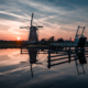 Windmühle und Zugbrücke in Kinderdijk bei Sonnenuntergang mit Spiegelungen auf der Wasseroberfläche